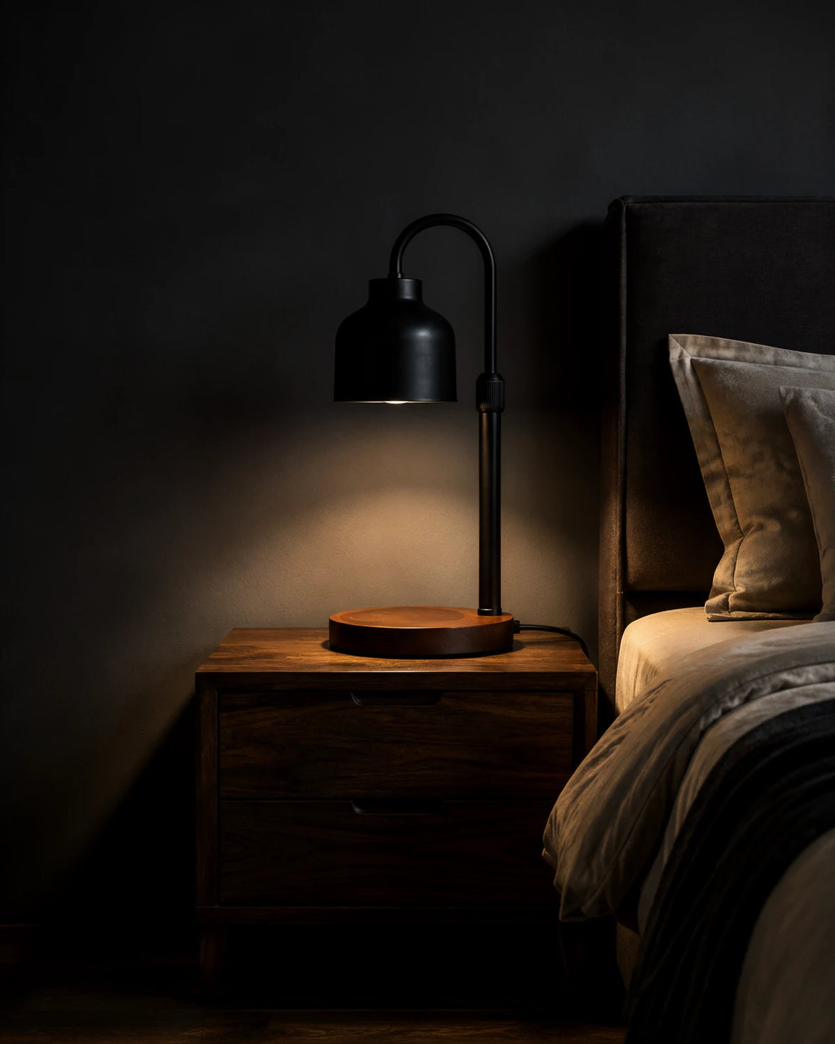 Black Nordic candle warmer lamp on a dark walnut nightstand beside a bed